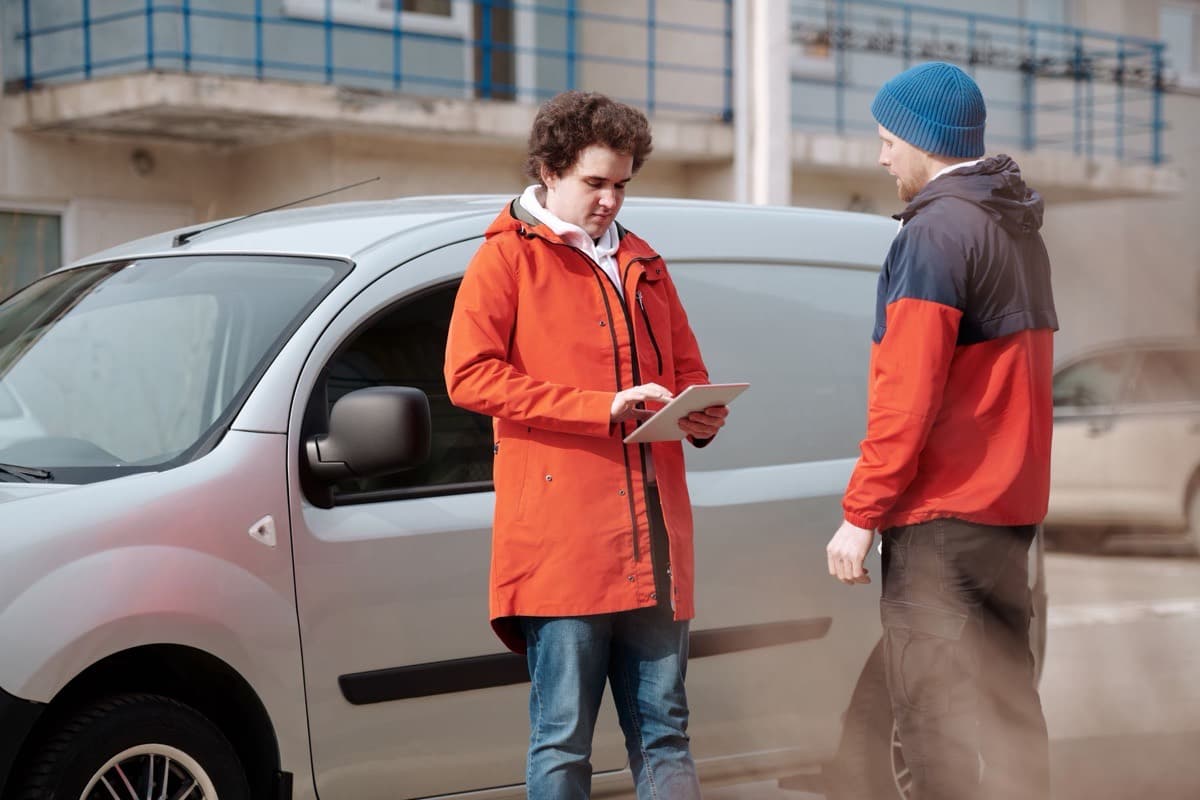 Deux personnes discutent devant une camionnette, une tablette à la main