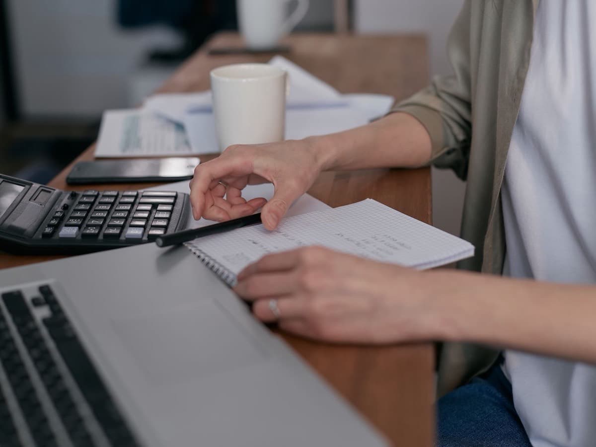 Des mains sur un ordinateur portable et une calculatrice, un café à côté