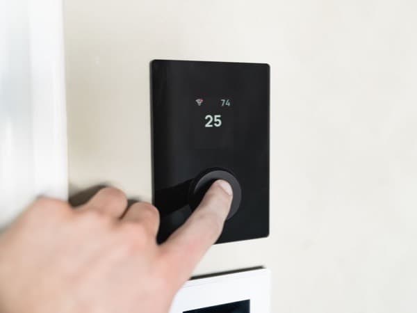 Main qui règle un thermostat noir au mur